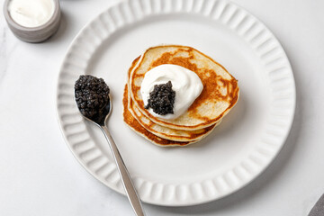 Black Caviar on pancakes with sour cream Holiday morning Appetizer on white plate and marble...