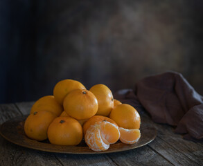 Tangerines in a vintage dish on a wooden surface. One tangerine is peeled. The dark key. Selective focus.