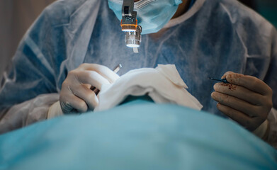 plastic surgeon operates on a patient with glasses and a flashlight in the operating room.