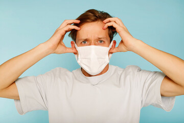 Young handsome man in white health care face mask standing with hand on head over blue background