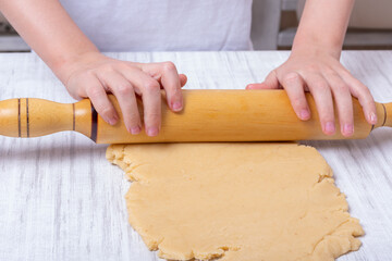 Children's hands roll out the dough with a rolling pin on the table in the kitchen. Little kid helps mother to cook