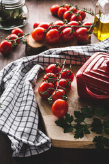 tomates cherry en rama sobre una mesa de madera, con una cacerola, un trapo de cocina y una tabla...