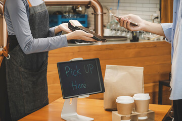 hand customer using digital mobile phone scan QR code pay buying coffee with waitress staff in apron and hot black coffee cup and dessert paper bag on desk in cafe coffee shop, cafe restaurant concept