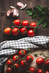 Vista superior de racimos de tomates cherry en rama en una mesa de madera, con ajo, perejil, una...