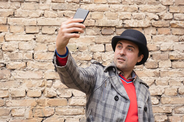 A man with a smartphone in his hands against a background of a brick wall.