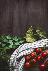 Vista superior de un racimo de tomates cherry con perejil, hojas de laurel, tomillo y un trapo de...