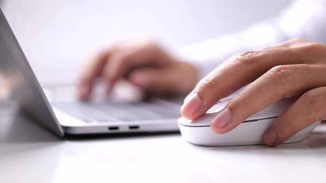 The male hand holds a computer mouse and typing laptop keyboard.