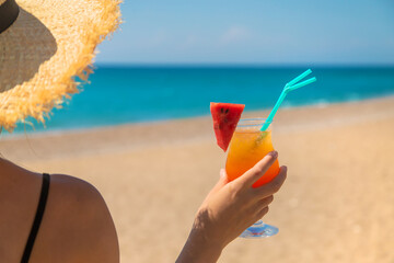 A woman holds a cocktail in her hand against the background of the sea. Selective focus.