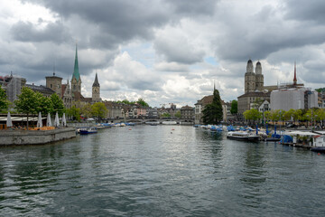 The Limmat River divides the cityscape of Zurich, Switzerland on a cloudy spring afternoon - the spires of churches and buildings rise and boats are docked on the water