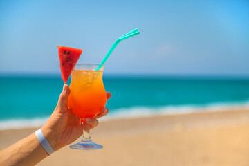 A woman holds a cocktail in her hand against the background of the sea. Selective focus.