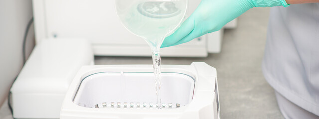 The beautician adds liquid for disinfection of instruments to the machine for sterilization of tools