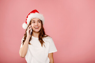Happy young teenager girl in Santa claus hat talking on the phone, cheerful woman enjoys pleasant mobile conversation, smiling millennial female holding cell speaking making call by telephone 