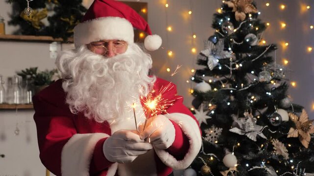 Happy Santa Claus is dancing with sparklers, enjoying music. Satna claus is having fun in room with Christmas tree. Happy, magical, children's, family holiday, Christmas. New Year, Christmas