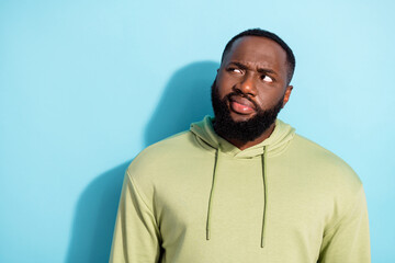 Photo of young contemplated guy sullen grimace look interested empty space isolated on blue color background