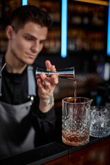 Bartender in apron adds ingredient to glass