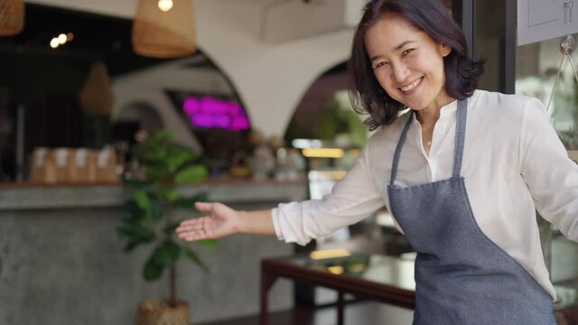 Asia latin adult female SME worker stand pride at front door work smile laugh look camera in new store small coffee shop. Happy casual day enter pub bar cafe warm hand sign for food drink industry.