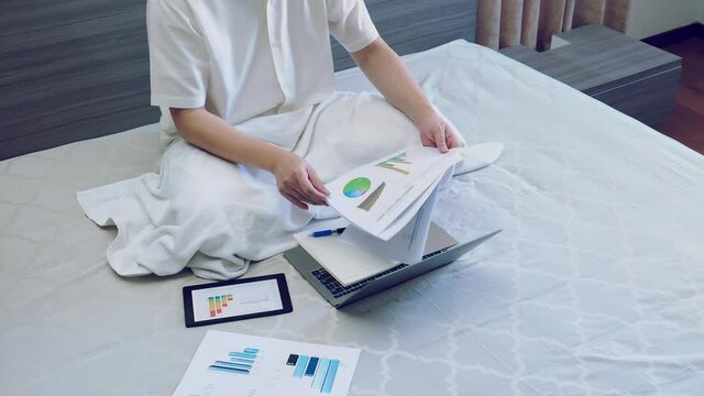 asian business man work with chart or graph report on bed, worker sits and works business on chart or graph for data analytics on bed at home - Powered by Adobe