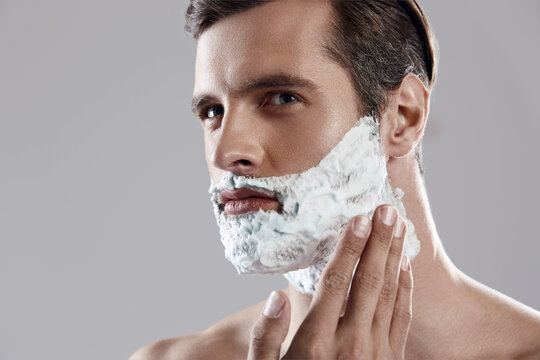 Serious man applying shaving foam on his face