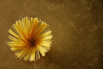 Italian durum wheat spaghetti, laid out in the shape of a blooming flower, on a dark brown textured stone table top. Free space for an inscription