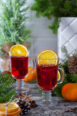 Festive arrangement of two glasses filled with aromatic mulled wine, complemented by sliced oranges, pinecones, and fir branches on a textured countertop.