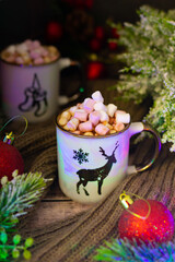 Warm mugs filled with creamy hot cocoa and marshmallows, adorned with festive deer and snowflake designs, nestled among holiday decor.