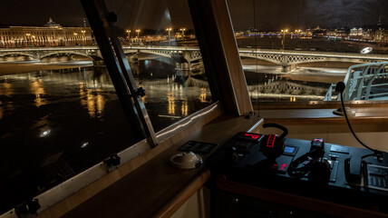The panoramic view from cabin of ship of the winter night city Saint-Petersburg with picturesque reflection on water, big ship moored near Blagoveshchensky bridge or lieutenant Schmidt