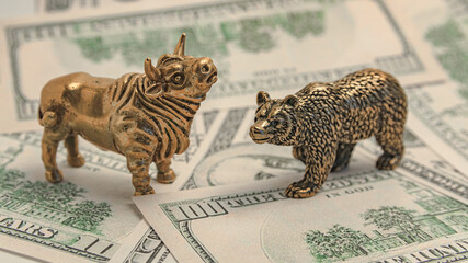 Figures of a bull and a bear made of yellow metal on the background of paper money. They symbolize...