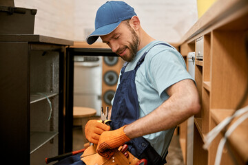 Cheerful repairman choosing tool to fix fridge