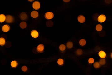 Defocused bokeh lights on black background, an abstract naturally blurred backdrop for Christmas eve or birthday party. Festive light texture. Yellow and red garland in blur. Overlay effect for design