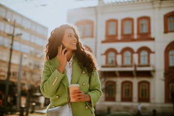 Fototapeta premium Young woman using smartphone on the street and holding takeaway coffee