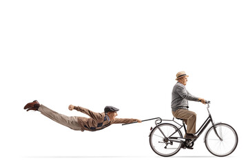 Elderly man riding a bicycle and other man flying behind