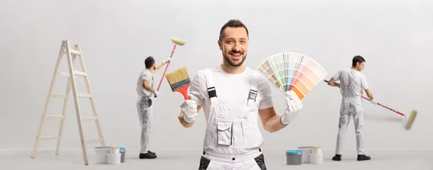 Foto op Aluminium House painter holding a color swatch palette and a brush and other painters painting a wall © Ljupco Smokovski