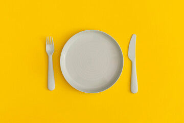 Blue plate with fork and spoon on a yellow background. Top view. Flat lay.