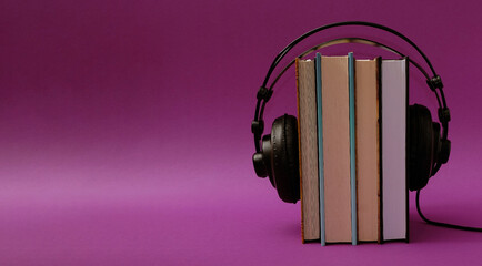 Black headphones hung from the top on books in an upright position on a violet background. Text...