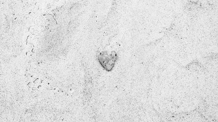 Heart-shaped gray sea rock on sandy beach, black and white photo