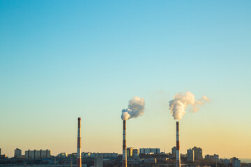 Three pipes from the CHP stand in the background of the city. The pipes release the products of combustion of fuel.