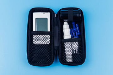 Home blood glucose test kit in carrying case on pastel blue background. Digital glucometer, lancet...