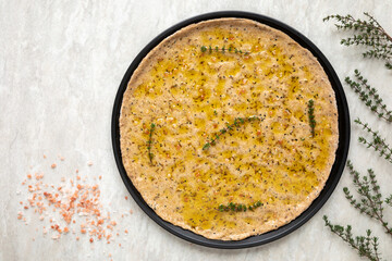 Unbaked focaccia round flat bread. Homemade pastry food with thyme herbs and salt top view.