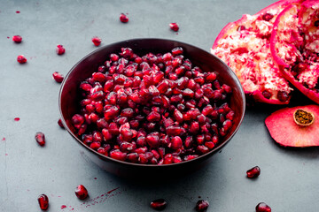 Bowl of Fresh Pomegranate Seeds on a Dark Background: A wooden bowl full of fresh pomegranate arils with a seeded fruit
