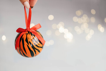 Christmas ball painted as tiger stripes spins on blurred christmas garland. background.  2022 is a year of the Tiger. Happy New Year . Symbol of year lunar chinese calendar tiger on Christmas  bal