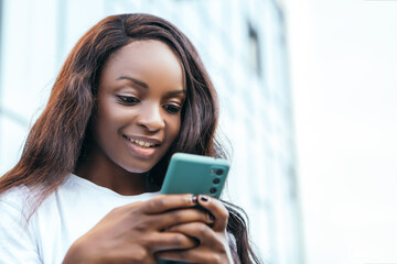 Smiling beautiful african american pretty woman hold hand phone surfing internet chatting friends colleague send message standing outside street blur bokeh background