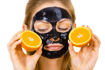 Girl black carbo mask on face holds orange fruit