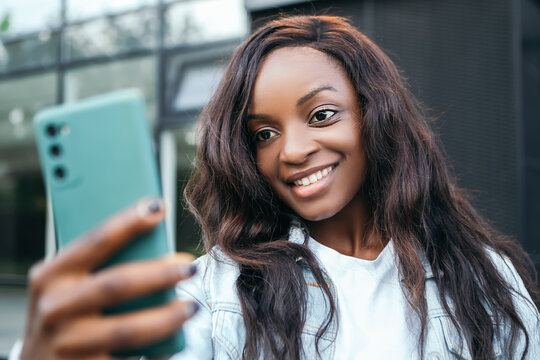 Smiling white teeth beautiful african american pretty woman hold hand phone chatting friends colleague relatives send message videochat standing outside street blur bokeh background