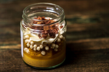 Dessert in a glass tub filled with cream cheese and caramel with white chocolate balls covered with dark chocolate and a crunchy biscuit base
