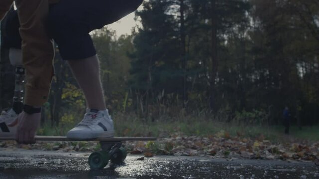 A young man with a metal bionic prosthetic leg is riding a skateboard in the autumn forest. An artificial leg pushes off the asphalt on a skateboard. A full life of a disabled person in the park.