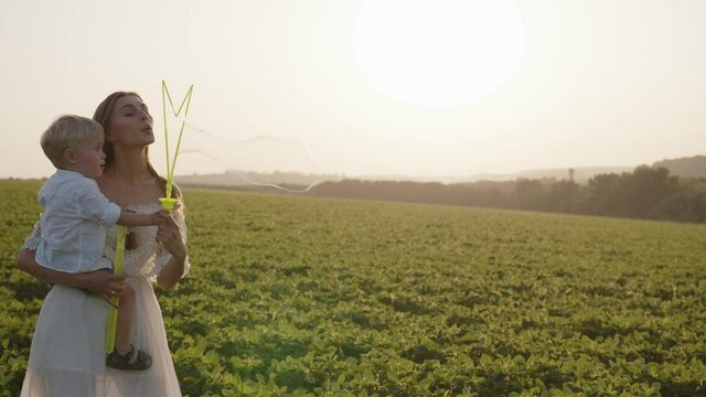 Beautiful mother with her son blow the bubles in a field