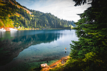 A woman is standing on a paddle board on the mountain lake