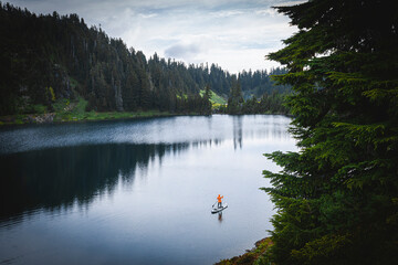 A woman is standing on a paddle board on the mountain lake