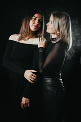 two beautiful elegant girls on a black background in black clothes close to each other