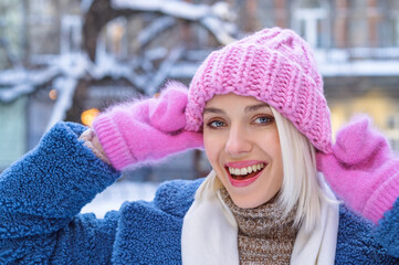 Happy smiling excited blonde woman wearing stylish pink knitted hat, mittens, posing in snow...